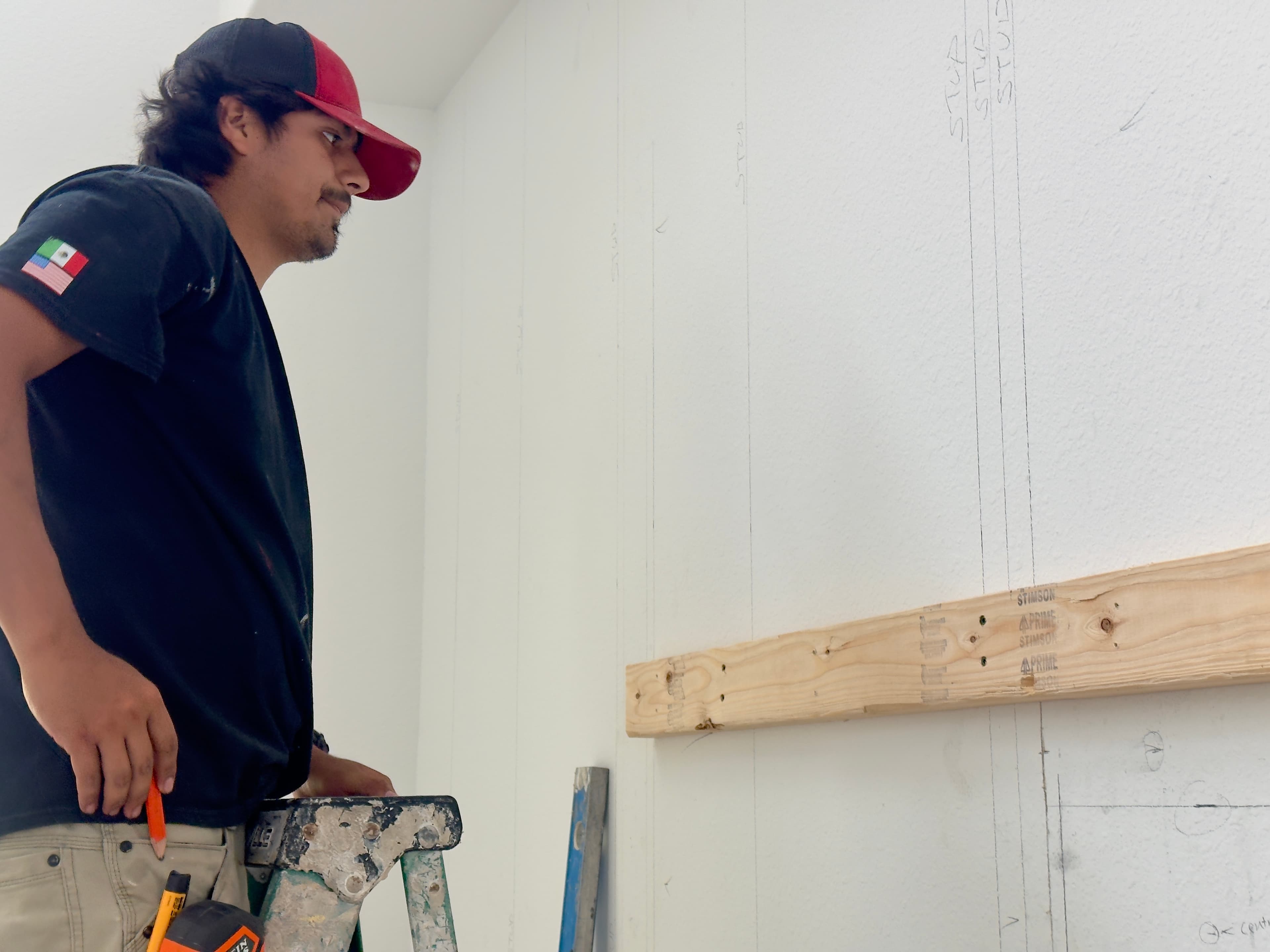 Houston tradesman on a ladder studying a wall marked with pencil stud lines mid-renovation